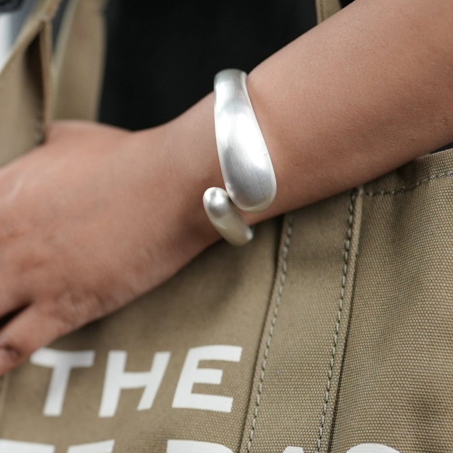 Elegant titanium finish statement bangle bracelet by Adiva Jewelry, styled on a woman's wrist with a neutral-toned sweater and canvas tote bag — a bold yet minimal accessory perfect for everyday sophistication.