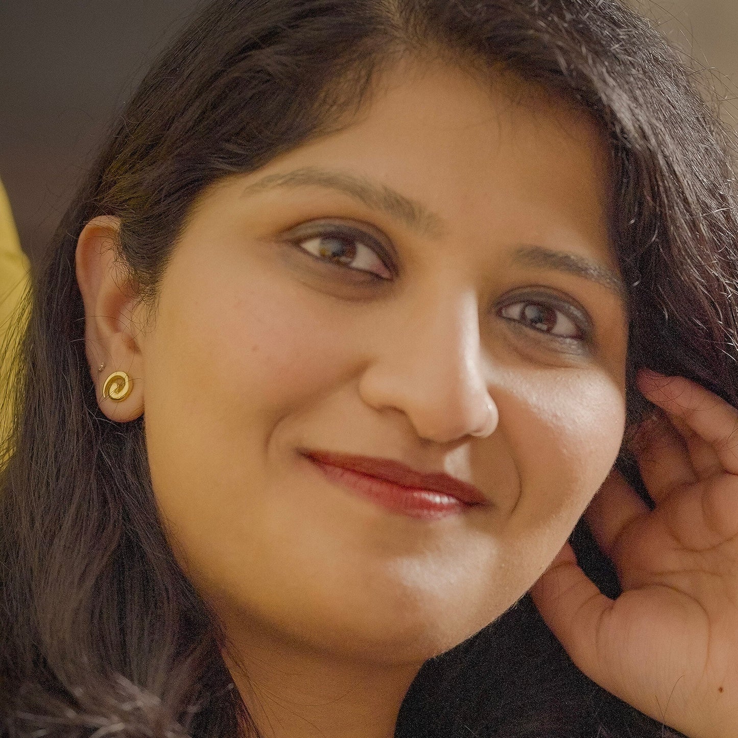 Woman wearing swirl shaped studs that are silver with gold plating