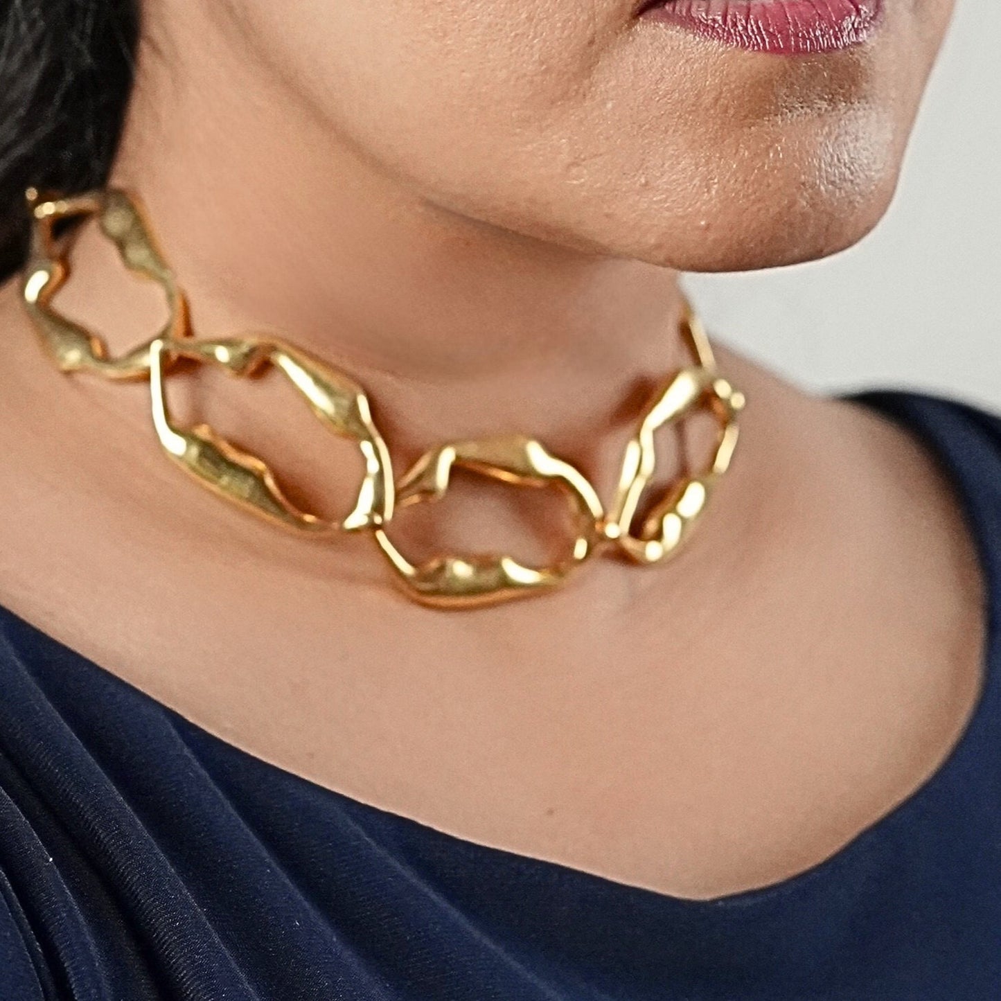 Woman wearing a sculpted chain necklace with a blue dress getting ready to go for a party, necklace made by Adiva Jewelry 
