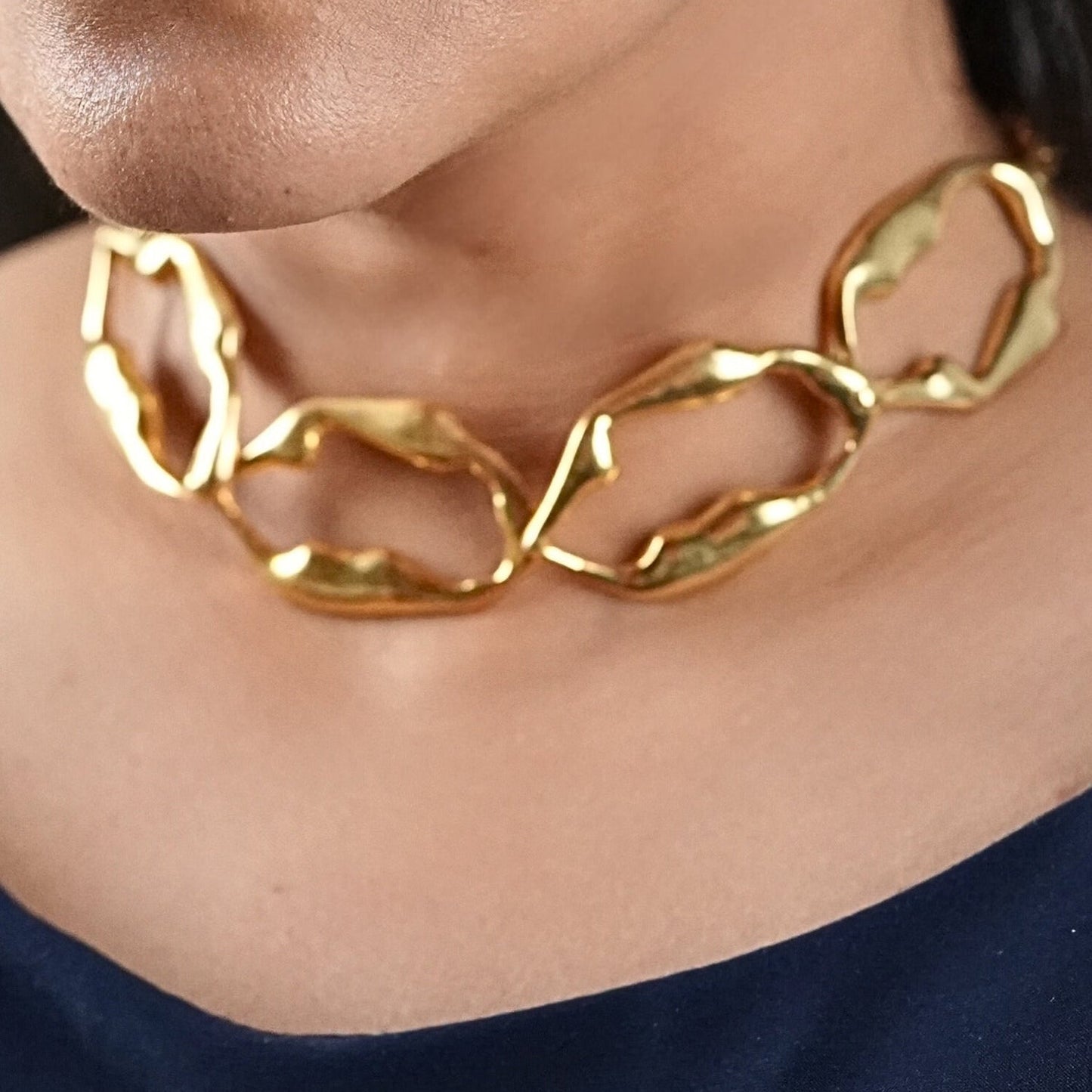 Woman in her 30s wearing a blue jumpsuit and a gold sculptural necklace that is skin friendly and artistic - made by Adiva Jewelry