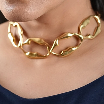 Woman in her 30s wearing a blue jumpsuit and a gold sculptural necklace that is skin friendly and artistic - made by Adiva Jewelry