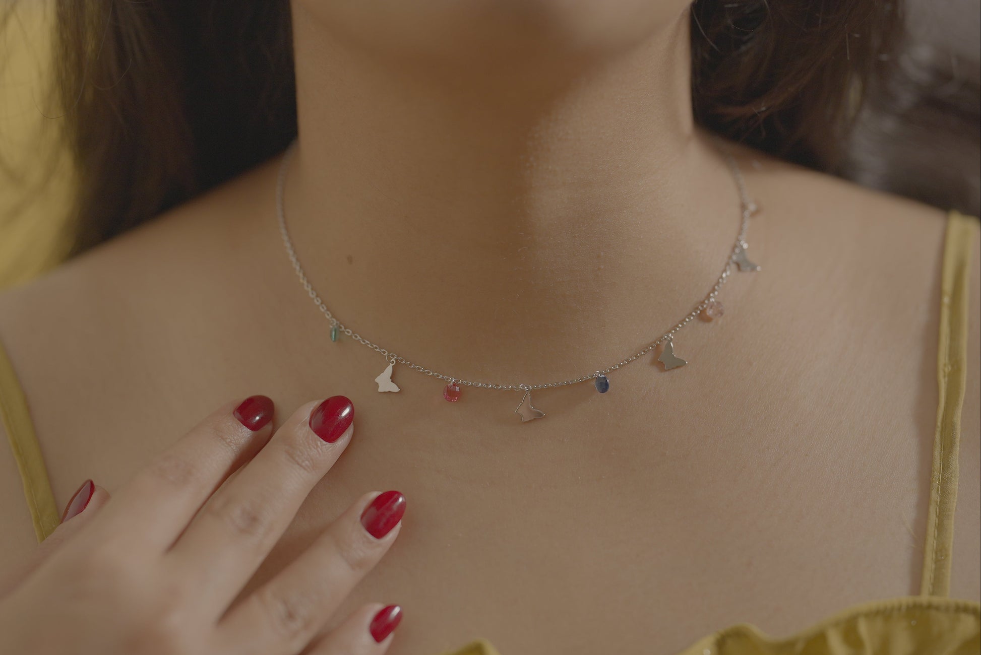 Close-up of a woman wearing a butterfly charm necklace made of touching her chest. Necklace is made of sterling silver and is by Adiva