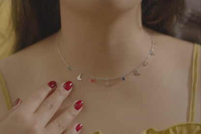 Close-up of a woman wearing a butterfly charm necklace made of touching her chest. Necklace is made of sterling silver and is by Adiva