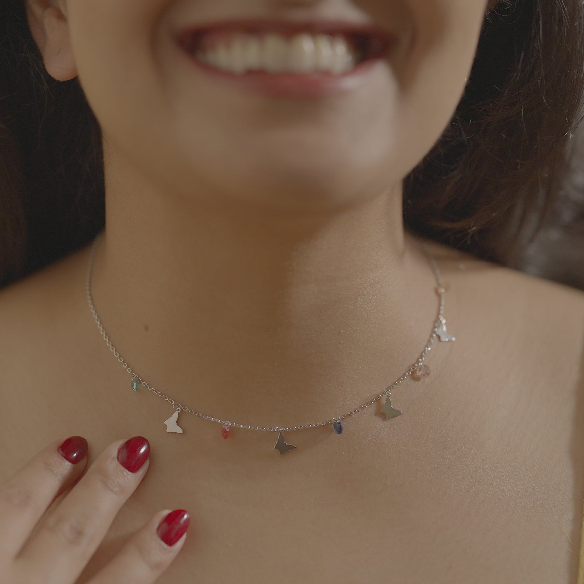 Close-up of a woman wearing a butterfly charm necklace made of touching her chest. Necklace is made of sterling silver and is by Adiva