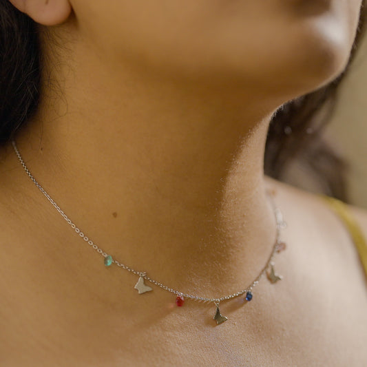 Close-up of a woman wearing a butterfly charm necklace made of touching her chest. Necklace is made of sterling silver and is by Adiva