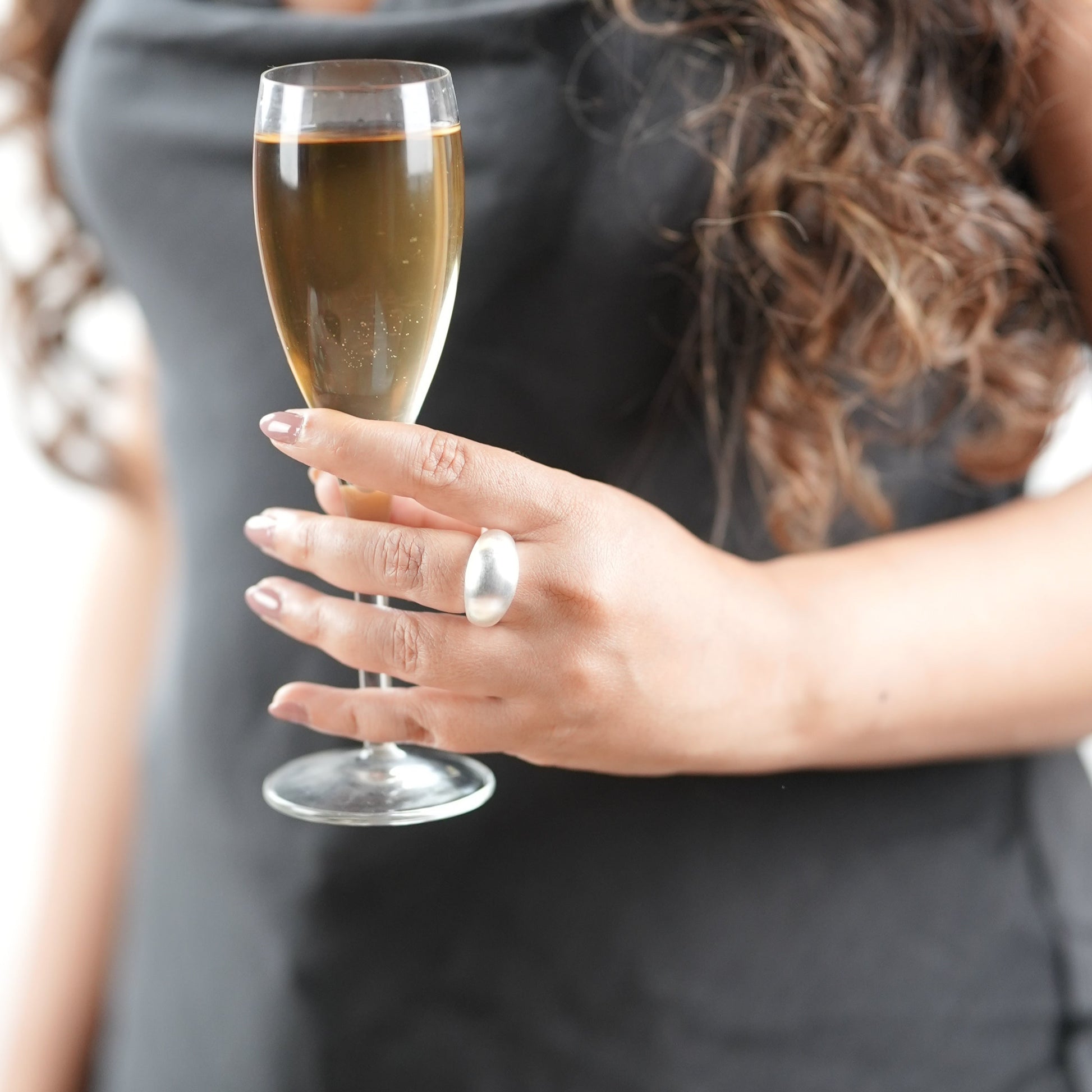 Bold matte silver statement ring on woman’s hand holding champagne flute – sculptural dome design, minimalist jewelry for modern women – Adiva Jewelry