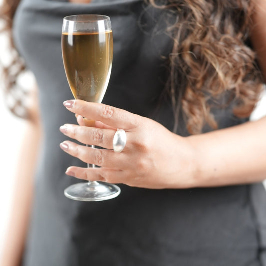 Bold matte silver statement ring on woman’s hand holding champagne flute – sculptural dome design, minimalist jewelry for modern women – Adiva Jewelry