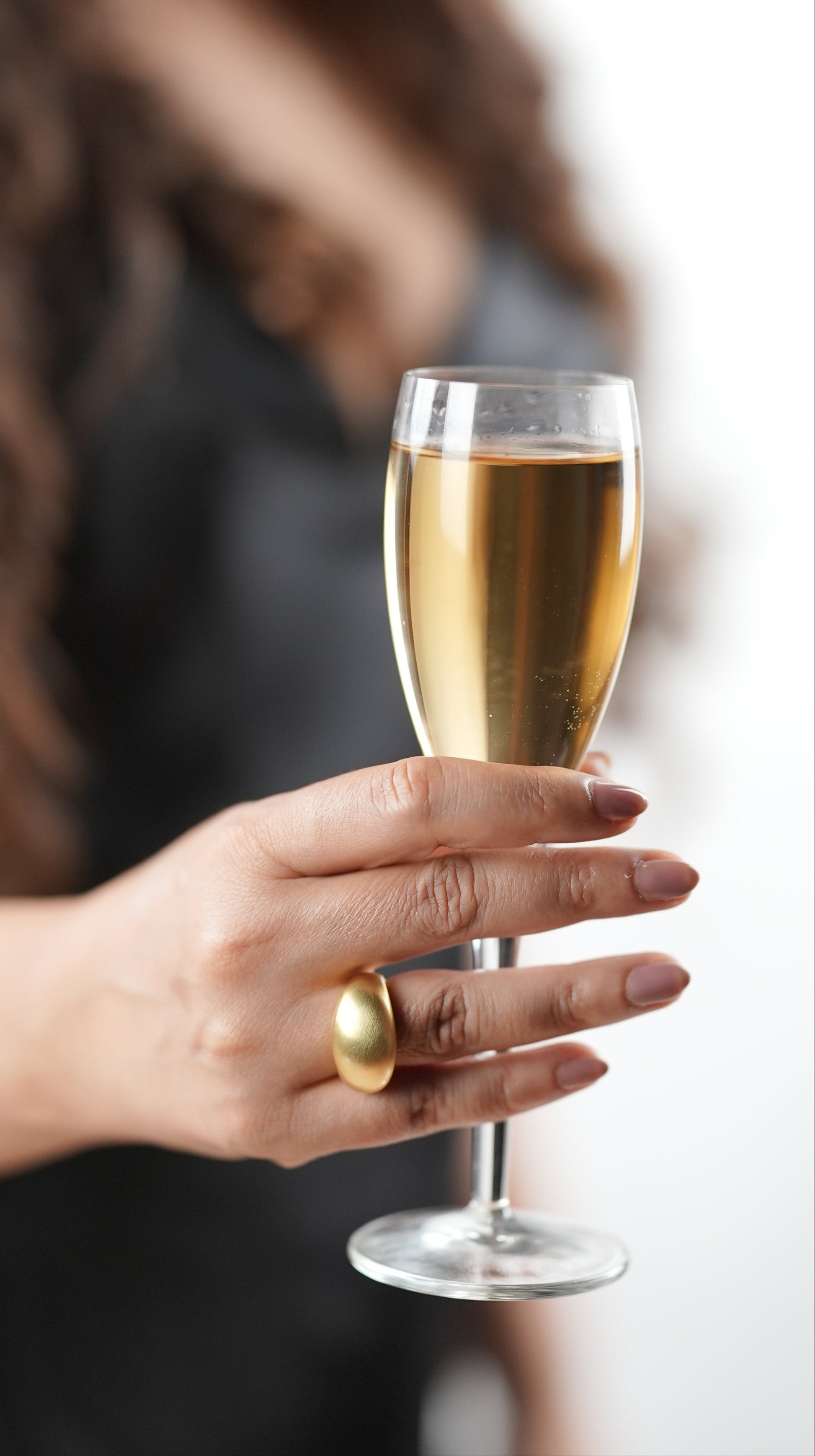 Bold satin gold statement ring on woman’s hand holding a champagne flute – minimalist sculptural cocktail ring, modern fashion accessory by Adiva Jewelry
