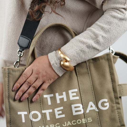 Elegant matt titanium finish gold-toned statement bangle bracelet by Adiva Jewelry, styled on a woman's wrist with a neutral-toned sweater and canvas tote bag — a bold yet minimal accessory perfect for everyday sophistication