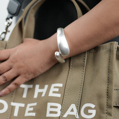 Elegant titanium finish statement bangle bracelet by Adiva Jewelry, styled on a woman's wrist with a neutral-toned sweater and canvas tote bag — a bold yet minimal accessory perfect for everyday sophistication.