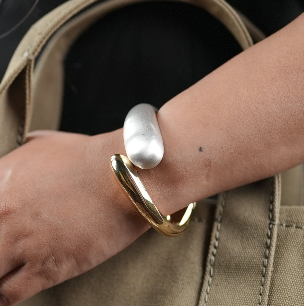 Statement dual-tone open cuff bracelet in silver and gold finish, worn on wrist holding khaki canvas tote bag – modern chunky jewelry for everyday fashion by Adiva Jewelry