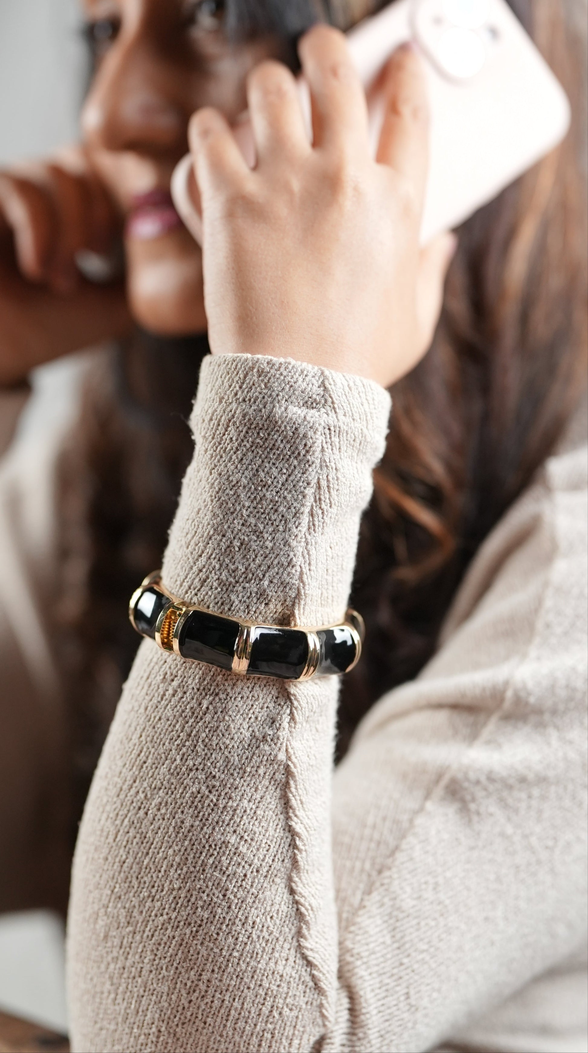 Black enamel and gold-toned segment bangle bracelet by Adiva Jewelry, styled on a woman's wrist as she talks on the phone — a bold, modern accessory perfect for workdays or evening elegance.