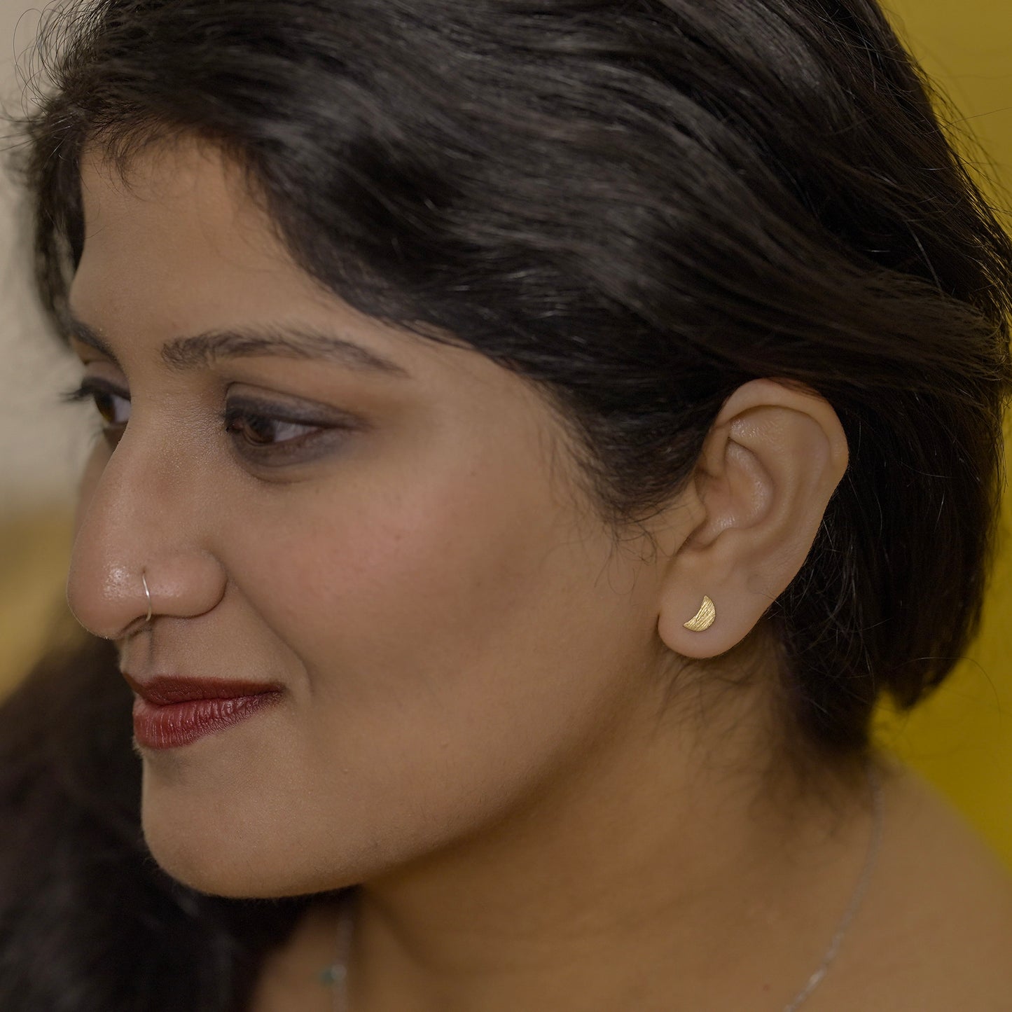 Close-up of a woman wearing a half moon earring made out of sterling silver and gold plating 