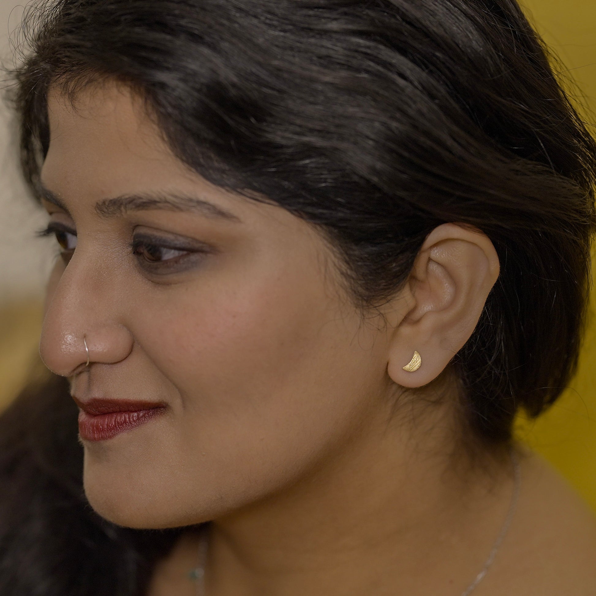 Close-up of a woman wearing a half moon earring made out of sterling silver and gold plating 