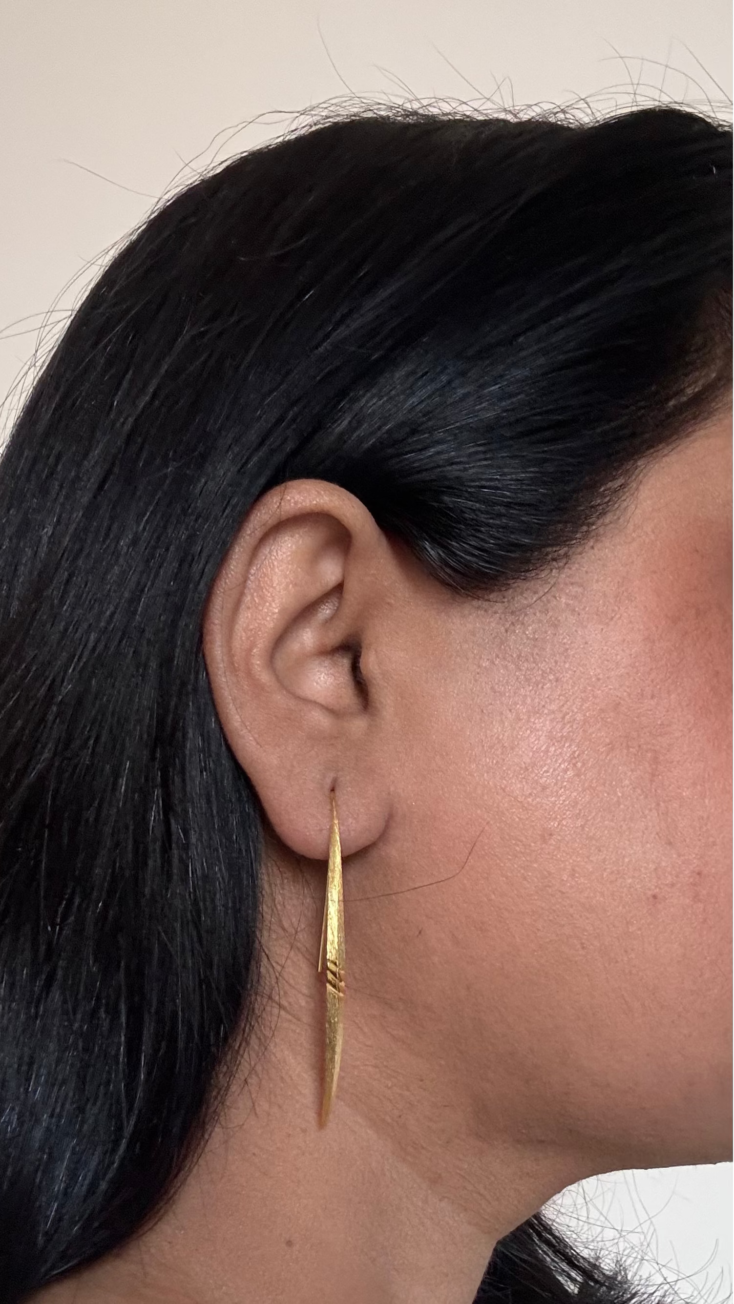 Close-up of a person wearing a gold hoop earring with a neutral background
