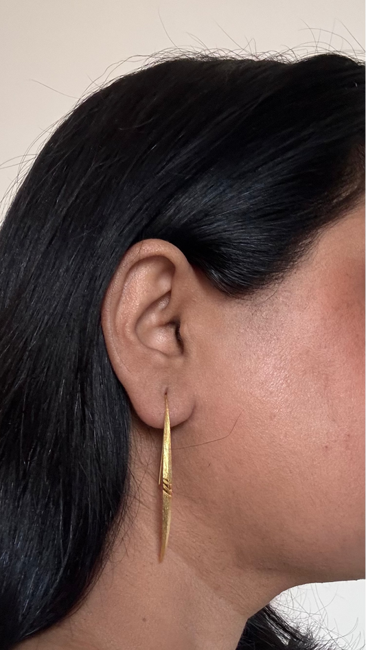 Close-up of a person wearing a gold hoop earring with a neutral background