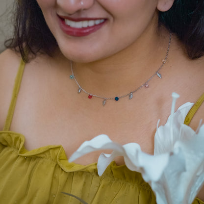 Close-up of a woman wearing a delicate necklace made of leaf and small colored stone charms touching her chest. Necklace is made of sterling silver and is by Adiva
